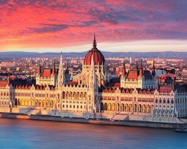 Mientras el sol se pone sobre Budapest durante "Un fin de semana en Budapest", el edificio del Parlamento húngaro ilumina un cielo impresionante, con sus reflejos brillando en el río Danubio. - ForTwo - Planes para parejas
