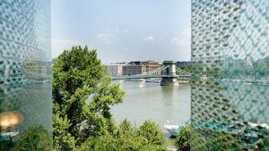 Con vistas al río de Budapest, un puente y un árbol delante de edificios altos bajo un cielo nublado: una escapada de pareja perfecta al hotel Lanchid 19 Design de Budapest. - ForTwo - Planes para parejas