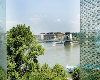 Con vistas al río de Budapest, un puente y un árbol delante de edificios altos bajo un cielo nublado: una escapada de pareja perfecta al hotel Lanchid 19 Design de Budapest. - ForTwo - Planes para parejas