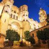 La histórica catedral, iluminada bajo el cielo nocturno con árboles que enmarcan su belleza, crea un escenario perfecto para una Escapada a Málaga en el Hotel del Pintor con entrada al museo Picasso. - ForTwo - Planes para parejas