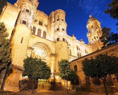 La histórica catedral, iluminada bajo el cielo nocturno con árboles que enmarcan su belleza, crea un escenario perfecto para una Escapada a Málaga en el Hotel del Pintor con entrada al museo Picasso. - ForTwo - Planes para parejas