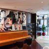 El paquete Escapadita a Budapest en pareja con hotel y desayuno incluye una estadía en un moderno lobby de hotel adornado con asientos naranjas, vibrantes retratos de arte en las paredes, exuberantes plantas y una elegante entrada de vidrio para un ambiente acogedor. - ForTwo - Planes para parejas