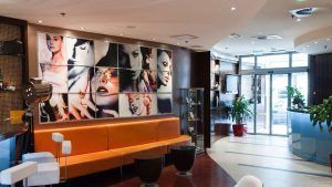 El paquete Escapadita a Budapest en pareja con hotel y desayuno incluye una estadía en un moderno lobby de hotel adornado con asientos naranjas, vibrantes retratos de arte en las paredes, exuberantes plantas y una elegante entrada de vidrio para un ambiente acogedor. - ForTwo - Planes para parejas