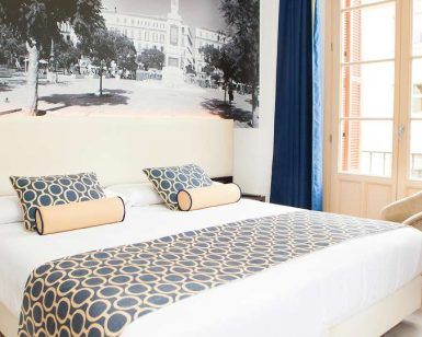 Descubra Escapada en el Hotel Soho Boutique (Málaga) en esta elegante habitación con una gran cama decorada con ropa de cama de diseño geométrico, un sillón y un distintivo mural en blanco y negro. Un acogedor refugio para su escapada a Málaga, enclavado en el corazón de la elegancia. - ForTwo - Planes para parejas