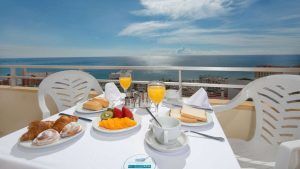 Disfrute de un desayuno sereno en un balcón con vistas al mar en Torremolinos, con frutas, bollería, tostadas y zumo de naranja sobre un mantel blanco impecable. La "Escapada de 3 días con todo incluido en Torremolinos" le garantiza tranquilidad y sabor para empezar el día con buen pie. - ForTwo - Planes para parejas