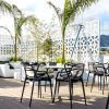 Un patio en la azotea con sillas negras, sofás blancos y palmeras ofrece el entorno perfecto para una escapada romántica en un hotel con jacuzzi y cena en Torremolinos. Relájese junto a la celosía decorativa en este tranquilo oasis bajo un cielo parcialmente nublado. - ForTwo - Planes para parejas