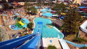 La vista aérea del Parque Acuático, cerca del hotel Las Palmeras, muestra toboganes vibrantes, piscinas cristalinas, palmeras exuberantes y visitantes disfrutando de las atracciones en la Escapada a Fuengirola con entradas al Parque Acuático. - ForTwo - Planes para parejas