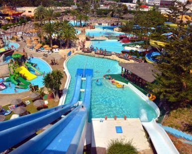 La vista aérea del Parque Acuático, cerca del hotel Las Palmeras, muestra toboganes vibrantes, piscinas cristalinas, palmeras exuberantes y visitantes disfrutando de las atracciones en la Escapada a Fuengirola con entradas al Parque Acuático. - ForTwo - Planes para parejas