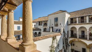 El patio blanco de estilo español de Escapada a Córdoba en el barrio judío, con balcones arqueados y techos de tejas, ofrece un refugio encantador bajo un cielo despejado, evocando el encanto de los barrios de Córdoba. - ForTwo - Planes para parejas