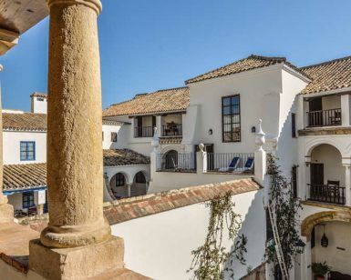 El patio blanco de estilo español de Escapada a Córdoba en el barrio judío, con balcones arqueados y techos de tejas, ofrece un refugio encantador bajo un cielo despejado, evocando el encanto de los barrios de Córdoba. - ForTwo - Planes para parejas