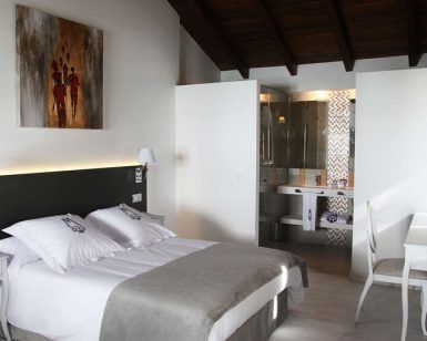 La Escapada en una casa señorial del siglo XVIII del Hotel La Casa del Médico en Córdoba ofrece una moderna habitación con cama doble, sábanas blancas, decoración artística y un baño abierto con paredes de cristal que realzan su elegante encanto. - ForTwo - Planes para parejas