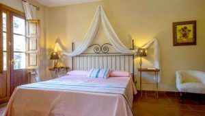 Disfrute de un acogedor refugio en el Hotel Humaina, con una colcha rosa, un cabecero ornamentado, mesitas de noche, lámparas y vistas a la montaña. Perfecto para una escapada a los Montes de Málaga, con un cuadro decorativo como toque final. - ForTwo - Planes para parejas