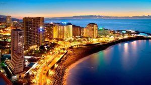 Perspectiva aérea del animado Puerto de la Cruz al atardecer, destacando sus imponentes estructuras y la serena costa del océano. Vívelo con la "Escapada al Puerto de la Cruz con pensión completa con hasta 1 niño gratis (Tenerife). - ForTwo - Planes para parejas