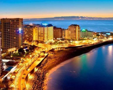Perspectiva aérea del animado Puerto de la Cruz al atardecer, destacando sus imponentes estructuras y la serena costa del océano. Vívelo con la "Escapada al Puerto de la Cruz con pensión completa con hasta 1 niño gratis (Tenerife). - ForTwo - Planes para parejas
