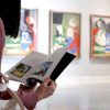 En el Museo Picasso Málaga, una persona se pierde en un libro, rodeada de pinturas abstractas, lo que proporciona un telón de fondo ideal para una escapada romántica llena de arte con la Escapada romántica a Málaga con entradas al museo Picasso: hotel María Cristina. - ForTwo - Planes para parejas