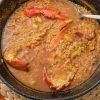 Una paella de mariscos con pimientos rojos y una cuchara para servir reposa sobre un salvamanteles tejido, capturando los vibrantes sabores del Restaurante Arrozeando (Málaga). Perfecto para disfrutar en este encantador restaurante malagueño. - ForTwo - Planes para parejas