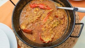 Una paella de mariscos con pimientos rojos y una cuchara para servir reposa sobre un salvamanteles tejido, capturando los vibrantes sabores del Restaurante Arrozeando (Málaga). Perfecto para disfrutar en este encantador restaurante malagueño. - ForTwo - Planes para parejas