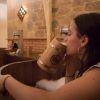 En un rústico Beer Spa de Tenerife, una mujer disfruta de una relajante bañera de madera mientras bebe de una taza también del mismo material. Otro huésped se relaja cerca, creando una experiencia idílica en el Circuito Beer Spa para dos que te transporta a la tranquilidad. - ForTwo - Planes para parejas