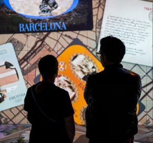 Dos personas admiran una exhibición de arte iluminada con texto e imágenes de Dragones y Modernismo en Barcelona: Experiencia inmersiva, que muestra el estilo modernista de Barcelona con cautivadores dragones míticos. - ForTwo - Planes para parejas