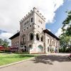 La impresionante mansión de piedra, que evoca al Hotel Castillo Del Bosque La Zoreda de Oviedo, cuenta con una torre rodeada de exuberantes jardines con un camino sinuoso bajo un cielo parcialmente nublado. - ForTwo - Planes para parejas