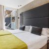 Moderna habitación con dos camas individuales en el Hotel Catalonia Giralda, con cabecero gris y manta verde. Balcón con vistas a la histórica Giralda a través de una ventana abierta con cortina. - ForTwo - Planes para parejas