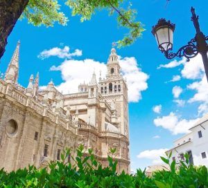 Experimente una vista impresionante de la icónica torre de la Giralda de la Catedral de Sevilla con su "Entrada para la Catedral de Sevilla y la Giralda (sin colas)", con un cielo azul como telón de fondo, una exuberante vegetación y acompañada de una encantadora farola vintage. - ForTwo - Planes para parejas