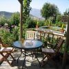 Disfrute de las pintorescas montañas de las Alpujarras desde el patio de su jardín en Apartamentos con cocina en las Alpujarras Cortijo Opazo (Granada), que cuenta con una mesa redonda de vidrio, dos sillas y flores vibrantes. - ForTwo - Planes para parejas