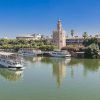El Crucero Torre del Oro por el Guadalquivir se desliza a lo largo del tranquilo río, con la histórica Torre del Oro y pintorescos edificios en el pintoresco telón de fondo bajo un cielo azul claro. - ForTwo - Planes para parejas