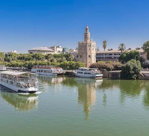 El Crucero Torre del Oro por el Guadalquivir se desliza a lo largo del tranquilo río, con la histórica Torre del Oro y pintorescos edificios en el pintoresco telón de fondo bajo un cielo azul claro. - ForTwo - Planes para parejas