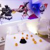 Una elegante habitación del Hotel Dormirdcine Madrid presenta una decoración blanca, un mural vibrante y detalles encantadores como naranjas y un sombrero en la cama. - ForTwo - Planes para parejas