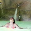 Una persona en una tranquila piscina de spa se relaja con los ojos cerrados, disfrutando del agua calmante de un chorro elevado, que recuerda a la experiencia del Circuito Termal Privado de Spa de 90 minutos en el Cercado de la Alpujarra. - ForTwo - Planes para parejas