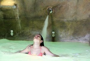 Una persona en una tranquila piscina de spa se relaja con los ojos cerrados, disfrutando del agua calmante de un chorro elevado, que recuerda a la experiencia del Circuito Termal Privado de Spa de 90 minutos en el Cercado de la Alpujarra. - ForTwo - Planes para parejas