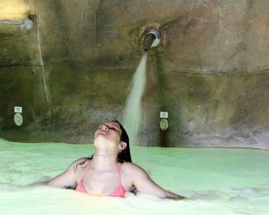 Una persona en una tranquila piscina de spa se relaja con los ojos cerrados, disfrutando del agua calmante de un chorro elevado, que recuerda a la experiencia del Circuito Termal Privado de Spa de 90 minutos en el Cercado de la Alpujarra. - ForTwo - Planes para parejas
