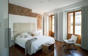Experimente el encanto de Eric Vökel Boutique Apartments en un dormitorio moderno con una pared con acento de ladrillo, ventanas grandes, una cama blanca impecable, pisos de madera cálidos y muebles minimalistas que crean un ambiente sereno. - ForTwo - Planes para parejas