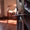 Una llave antigua en una antigua cerradura de puerta de madera evoca una sensación de misterio, similar al Escape Room Resuelve el Misterio del Hotel en Zafra, con un fondo borroso de una silla y una ventana que añade elegancia. - ForTwo - Planes para parejas