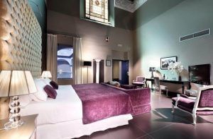Descubra la elegancia de una habitación en el Hotel Eurostars Sevilla Boutique, equipada con una gran cama, detalles en morado, una decoración sofisticada y una impresionante vidriera. - ForTwo - Planes para parejas