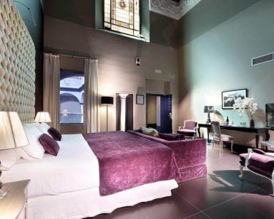 Descubra la elegancia de una habitación en el Hotel Eurostars Sevilla Boutique, equipada con una gran cama, detalles en morado, una decoración sofisticada y una impresionante vidriera. - ForTwo - Planes para parejas