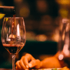 El vino tinto, rico y aterciopelado, se vierte expertamente en una copa en medio de una iluminación cálida y un fondo borroso, creando una atmósfera íntima similar a la "Excursión y Cata de Vinos de la Ribera del Duero desde Madrid". - ForTwo - Planes para parejas