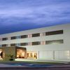 Bajo un cielo nublado por la noche, el Hotel Las Bóvedas en Badajoz impresiona con su diseño moderno y su icónico letrero H brillante. Para una experiencia inolvidable, considere el exclusivo Paquete Romántico en Hotel Las Bóvedas 4 estrellas. - ForTwo - Planes para parejas