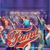 Artistas con trajes vibrantes saltan al escenario del Teatro EDP Gran Vía, con el texto "Fama, el musical" superpuesto. - ForTwo - Planes para parejas