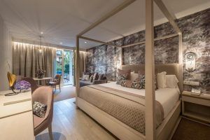 Disfrute de la elegante habitación del Gran Hotel Miramar Málaga, equipada con cama con dosel, sofá y escritorio. Relájese en el balcón con una serena vista al jardín y una relajante decoración en tonos neutros. - ForTwo - Planes para parejas