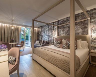 Disfrute de la elegante habitación del Gran Hotel Miramar Málaga, equipada con cama con dosel, sofá y escritorio. Relájese en el balcón con una serena vista al jardín y una relajante decoración en tonos neutros. - ForTwo - Planes para parejas