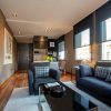 Una moderna sala de estar con sofás oscuros, una mesa de centro de cristal, zona de comedor y grandes ventanales que ofrecen una vista de la ciudad que recuerda a la Grand Suite: la joya de la corona del Grand Hotel Central de Barcelona. - ForTwo - Planes para parejas