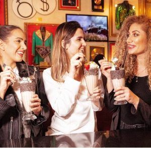 Tres mujeres saborean batidos en el Hard Rock Café Barcelona, sonriendo y charlando en medio de un ambiente bellamente decorado. - ForTwo - Planes para parejas