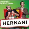 Dos hombres sostienen un cartel con la leyenda "Hernani" sobre un fondo verde. Uno de ellos sostiene con orgullo una bandera española, capturando la vibrante energía asociada a Hernani en el Teatro Lara de Madrid. Texto: Una comedia... - ForTwo - Planes para parejas