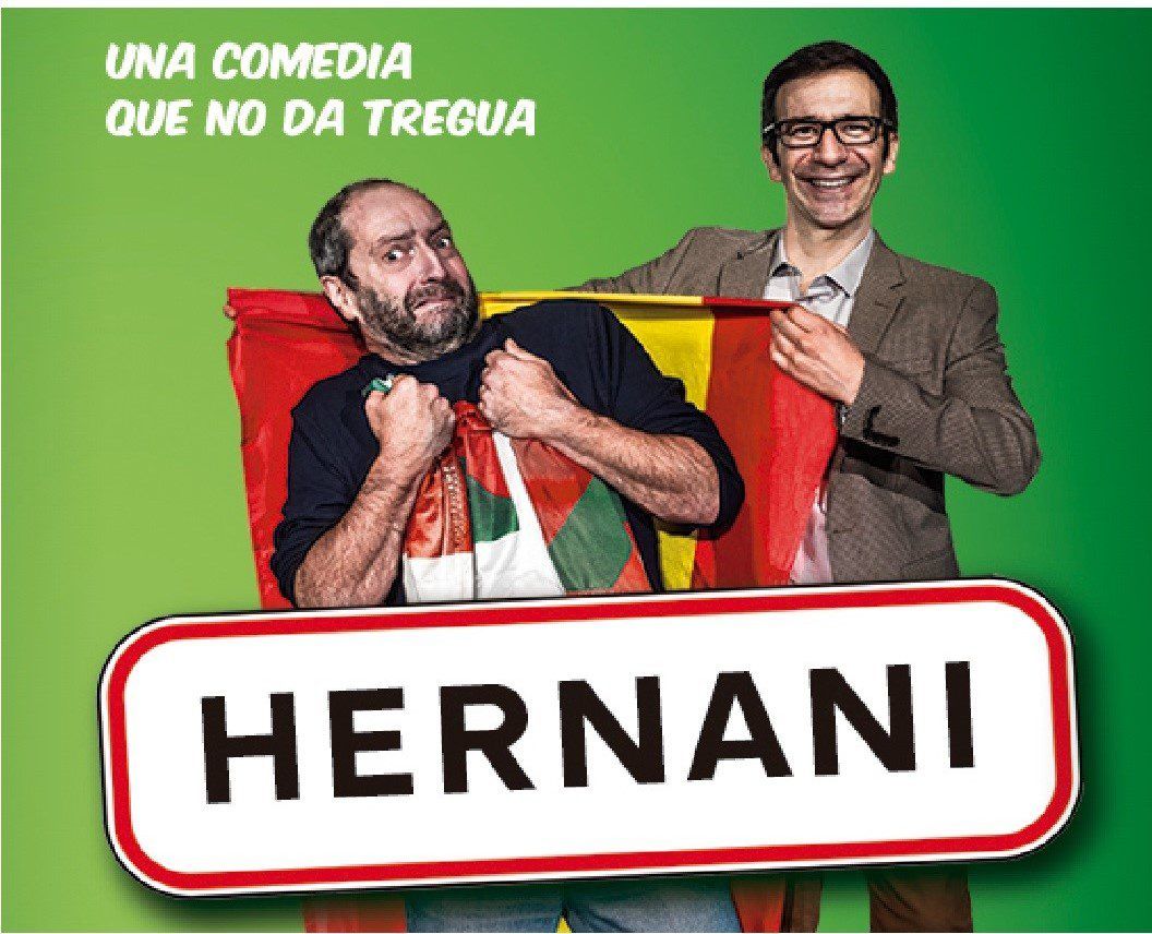 Dos hombres sostienen un cartel con la leyenda "Hernani" sobre un fondo verde. Uno de ellos sostiene con orgullo una bandera española, capturando la vibrante energía asociada a Hernani en el Teatro Lara de Madrid. Texto: Una comedia... - ForTwo - Planes para parejas