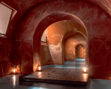 Un pasillo arqueado con iluminación tenue que recuerda a la Experiencia Hammam Tradicional - Baño Turco en Madrid, con paredes estampadas y linternas que proyectan cálidos reflejos de luz en el suelo. - ForTwo - Planes para parejas