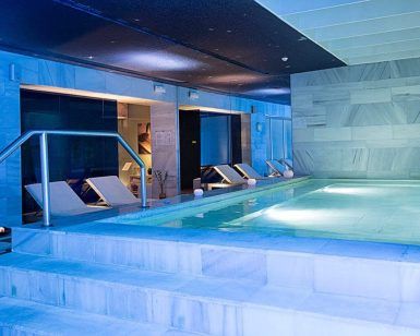 El Spa del Hospes Palacio de los Patos en Granada cuenta con una piscina cubierta con tumbonas, una relajante iluminación azul y un interior de mármol para un ambiente sereno. - ForTwo - Planes para parejas
