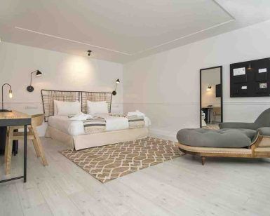 Ubicada en el Hotel 7 Islas Madrid, esta habitación minimalista incluye una cómoda cama, un televisor montado en la pared, un escritorio elegante, un cómodo sillón y una elegante alfombra sobre un piso de madera clara. - ForTwo - Planes para parejas