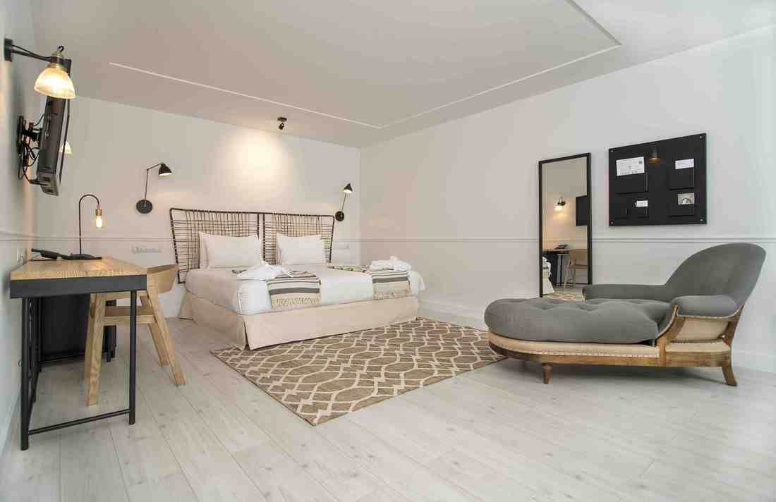 Ubicada en el Hotel 7 Islas Madrid, esta habitación minimalista incluye una cómoda cama, un televisor montado en la pared, un escritorio elegante, un cómodo sillón y una elegante alfombra sobre un piso de madera clara. - ForTwo - Planes para parejas